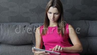 穿裙子的女人<strong>坐在沙发</strong>上用平板电脑。 <strong>坐在沙发</strong>上用平板电脑工作的女孩